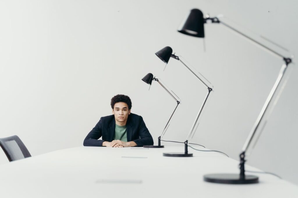 Young professional man seated at a long desk in a modern office with multiple lamps.